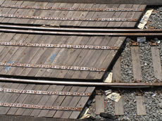 A railroad track crossover with over a dozen wooden ties lined up next to each other, at an angle under the tracks